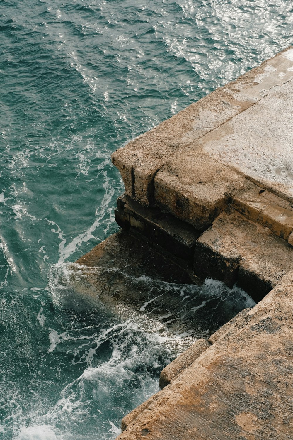 a person standing on a ledge near the ocean