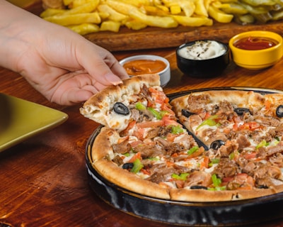 A hand reaching for a slice from a large two-topping pizza with vibrant vegetables and pepperoni.