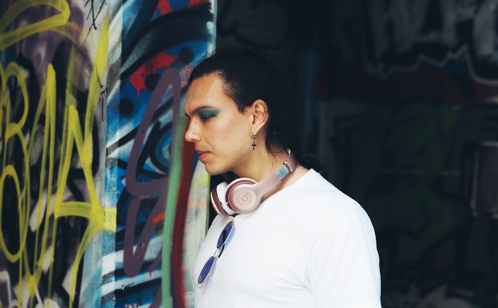a woman wearing headphones standing in front of a graffiti covered wall
