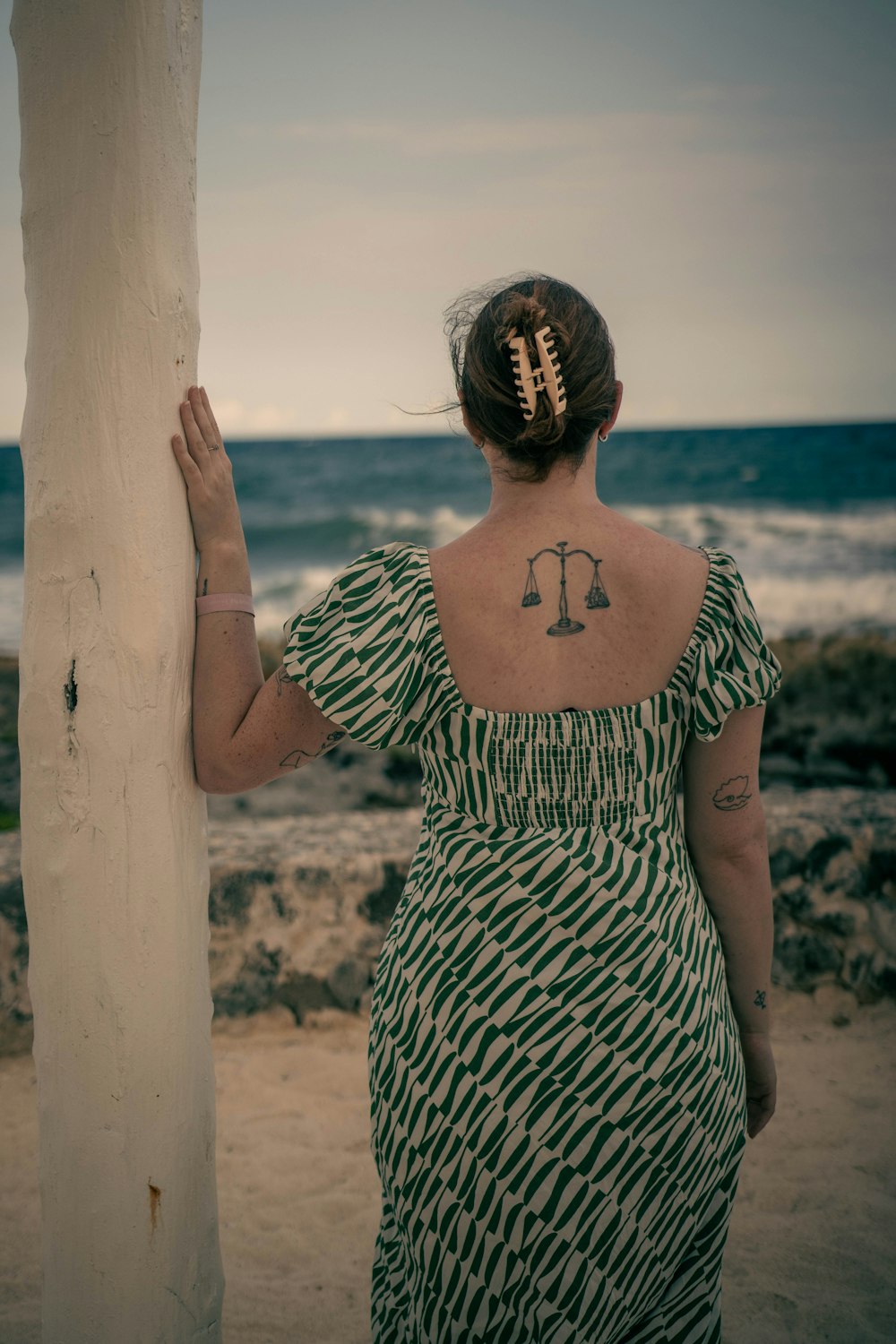 a woman with a tattoo on her back standing next to a pole