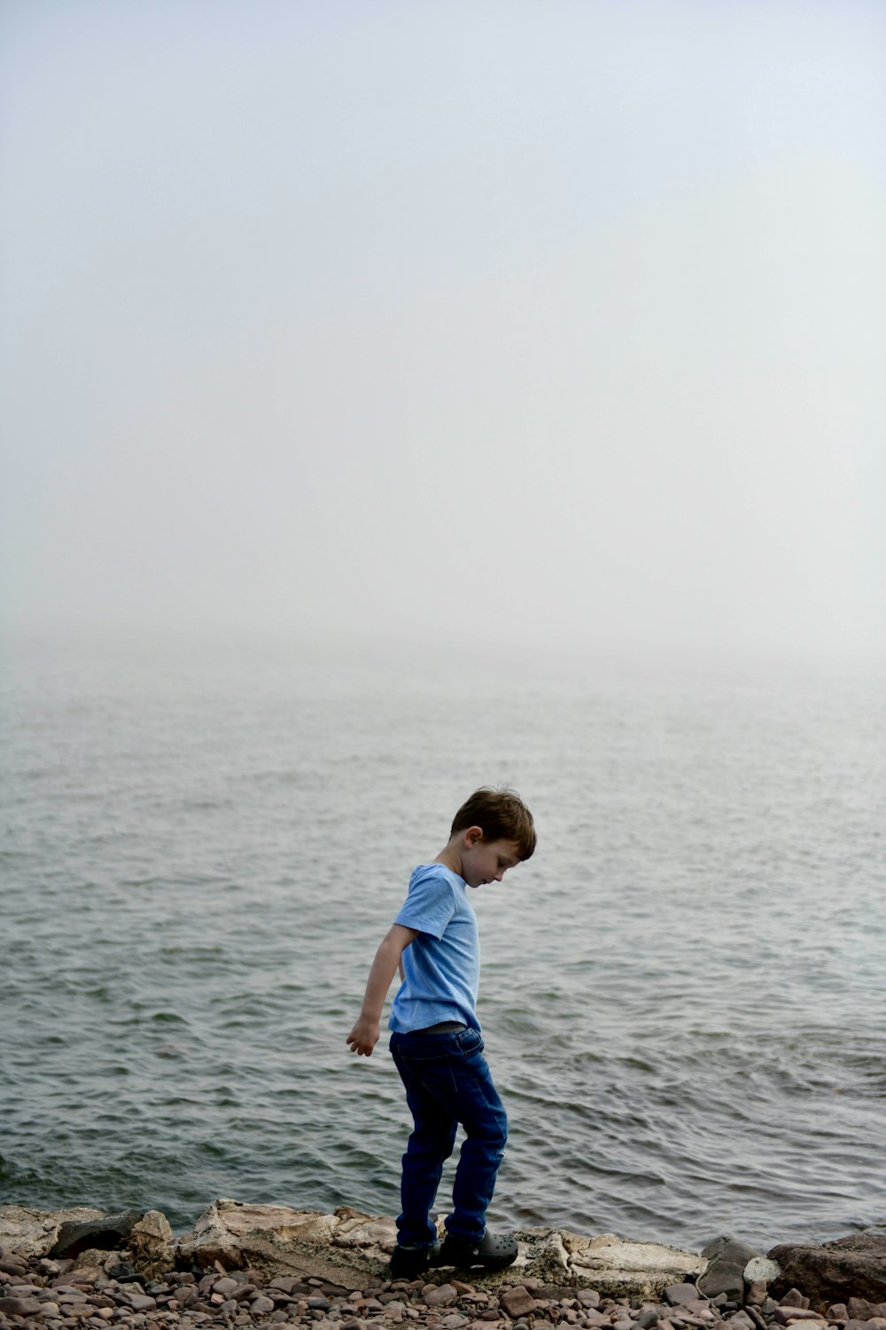 a young boy standing on top of a rocky beach