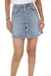 A person wearing a denim skirt with buttons down the front and a white top. The image focuses on the midsection, showing a wristwatch on the left arm.