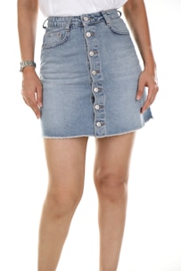 A person wearing a denim skirt with buttons down the front and a white top. The image focuses on the midsection, showing a wristwatch on the left arm.