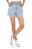 A person wearing blue and white pinstriped denim shorts paired with white sneakers that have blue accents. The shorts have a high waist with a ruffled edge and are fastened with buttons. The person’s hands are in the pockets of the shorts.