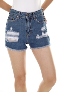 Blue denim shorts with frayed edges and distressed detailing. A white shirt is partially visible at the top, and bare legs are prominent in the image.