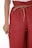 A close-up view of a person wearing loose-fitting red pants with a drawstring waistband. The pants have a crinkled texture, and the drawstring is made of a natural fiber material. The person’s hand is partially visible, resting on the side of the pants.