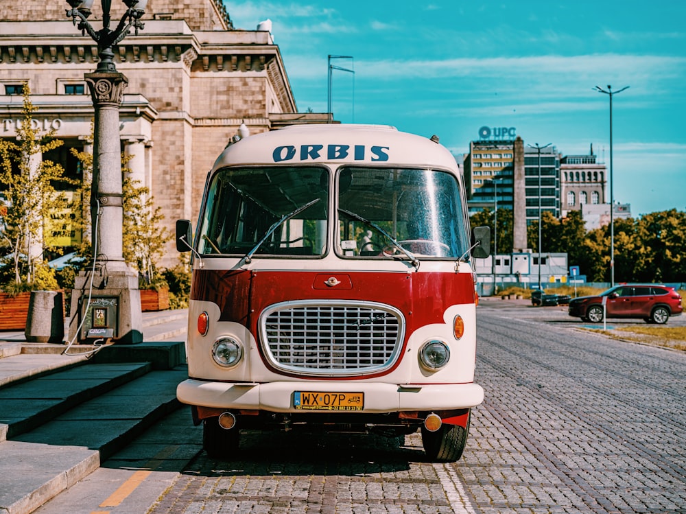 a red and white bus parked in front of a building