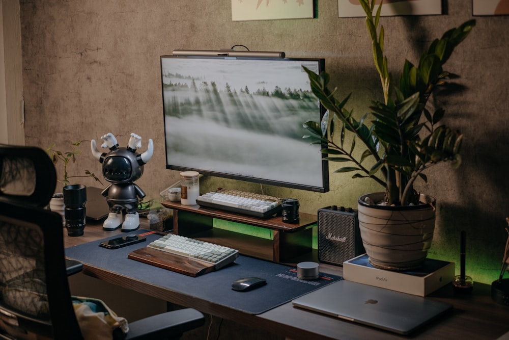 a desk with a computer monitor, keyboard and a plant