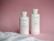 Two white bottles of Keune hair care products, including a conditioner and a shampoo, are placed against a pink backdrop. A white towel is partially visible in the foreground.