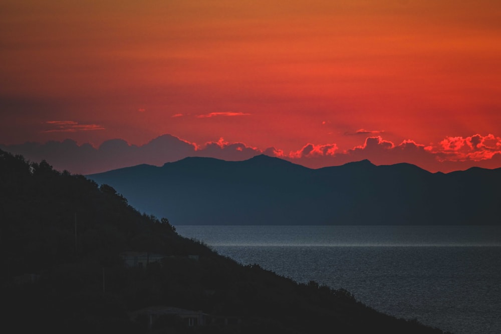 the sun is setting over the mountains by the water