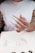 A hand with long, pointed nails, featuring a rainbow-colored design on two of the nails. The person is wearing a white shirt with a patterned sleeve visible. The hand displays a decorative ring with multiple gemstones. Below the hand is a sheet of paper with sketches or diagrams, suggesting a creative or design-oriented context.
