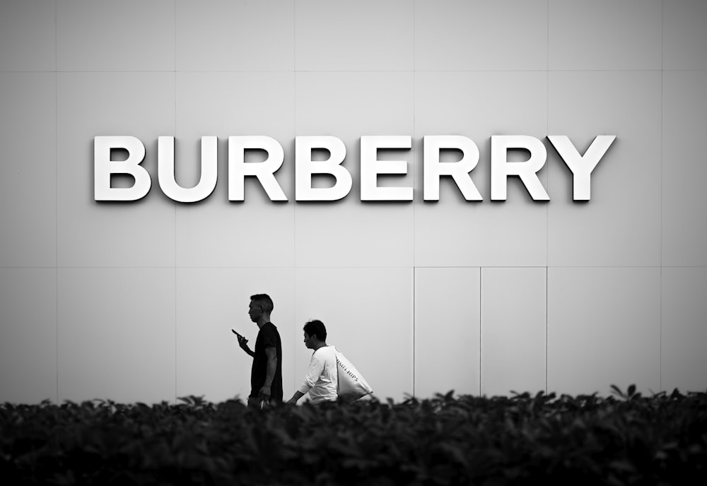 a couple of people walking past a burberry sign