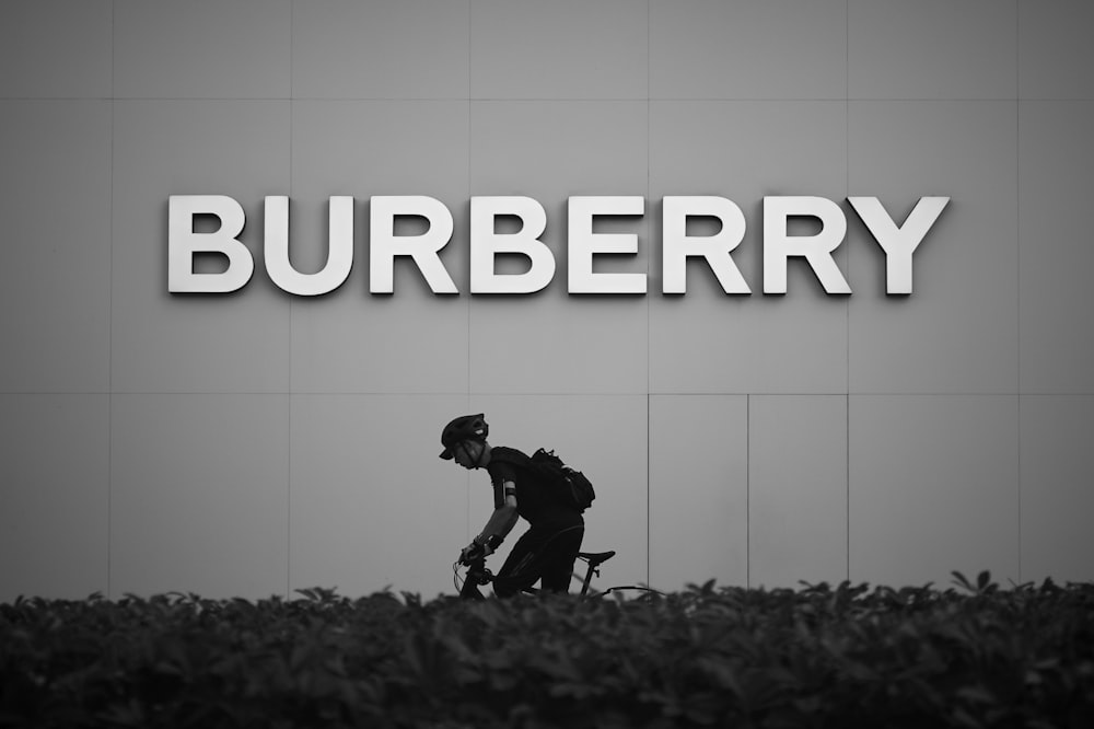 a black and white photo of a man riding a bike in front of a bu