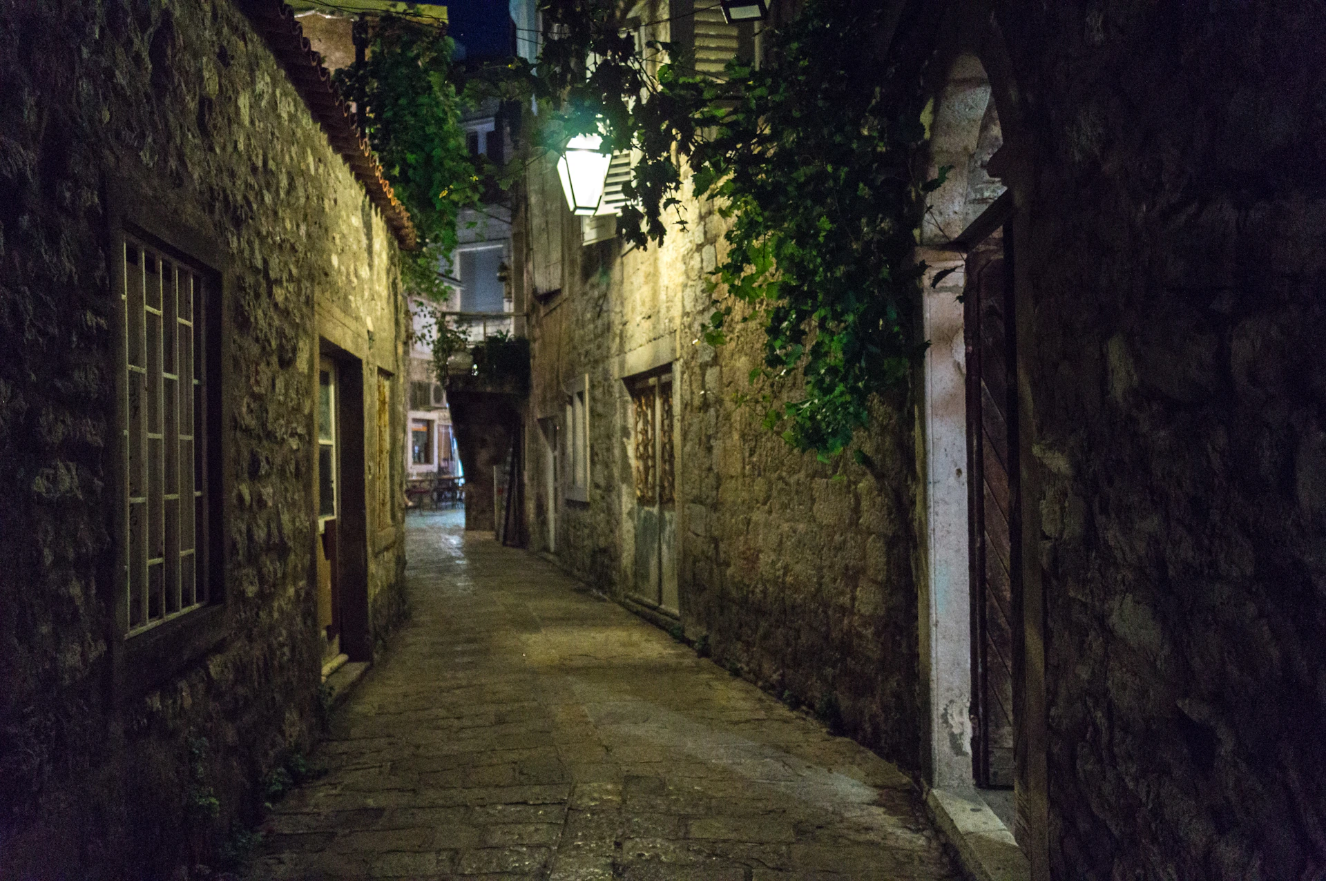 A quiet cobblestone alley lined with ivy-covered walls and warm lanterns glowing softly at dusk.