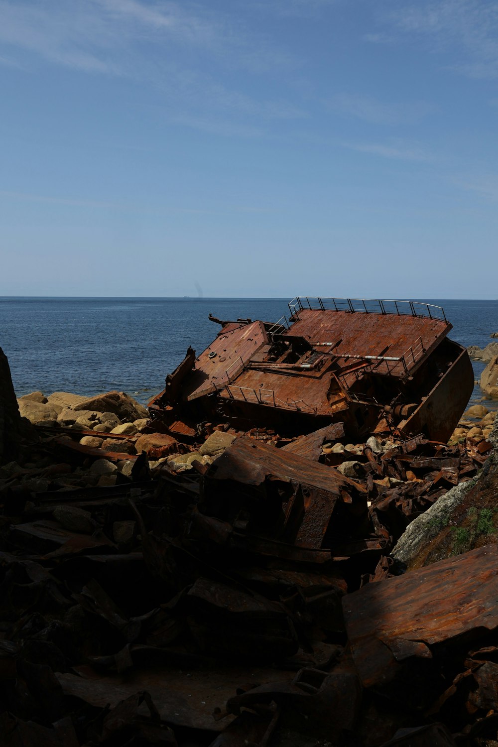 a rusted out boat sitting on top of a rocky beach