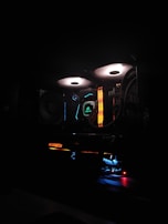 A computer setup is illuminated with colorful LED lights. The components, such as cooling fans with white light rings and RGB elements, create a vibrant and high-tech atmosphere. Various hardware brands are visible, with emphasis on aesthetic lighting.