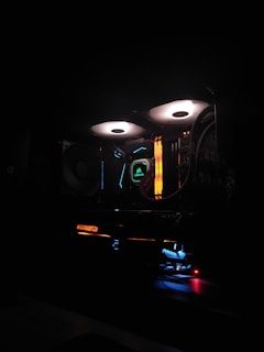A computer setup is illuminated with colorful LED lights. The components, such as cooling fans with white light rings and RGB elements, create a vibrant and high-tech atmosphere. Various hardware brands are visible, with emphasis on aesthetic lighting.