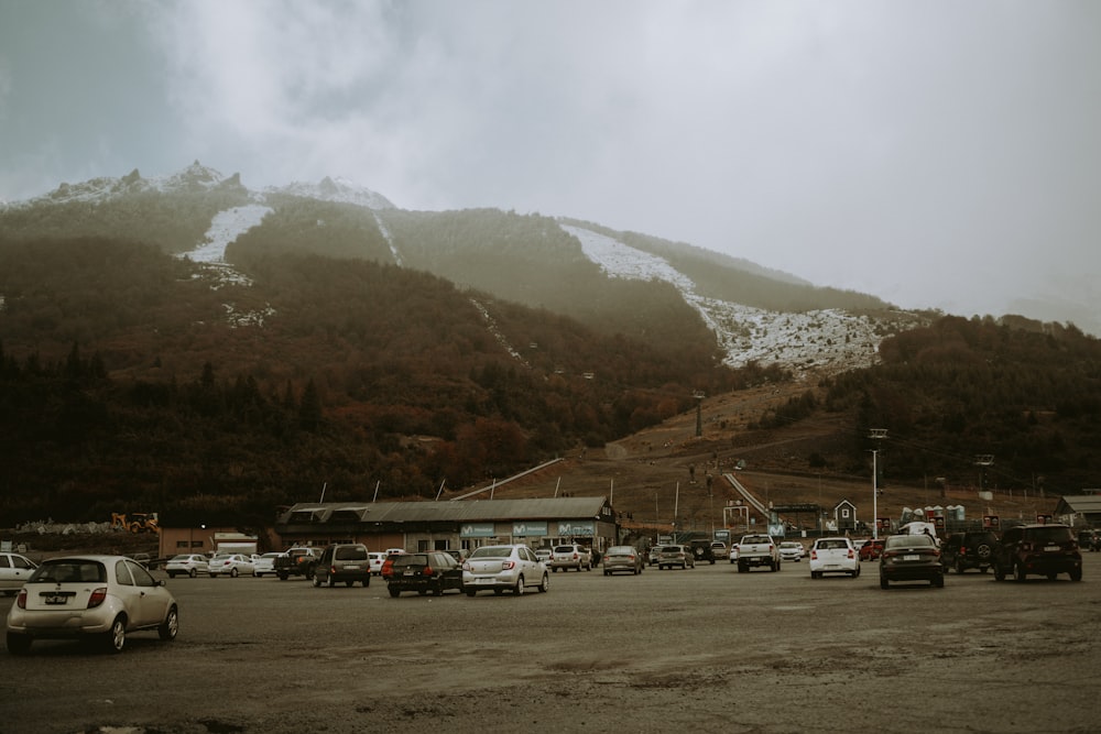 a parking lot filled with lots of cars next to a snow covered mountain