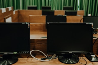 a row of computer monitors sitting on top of a wooden desk