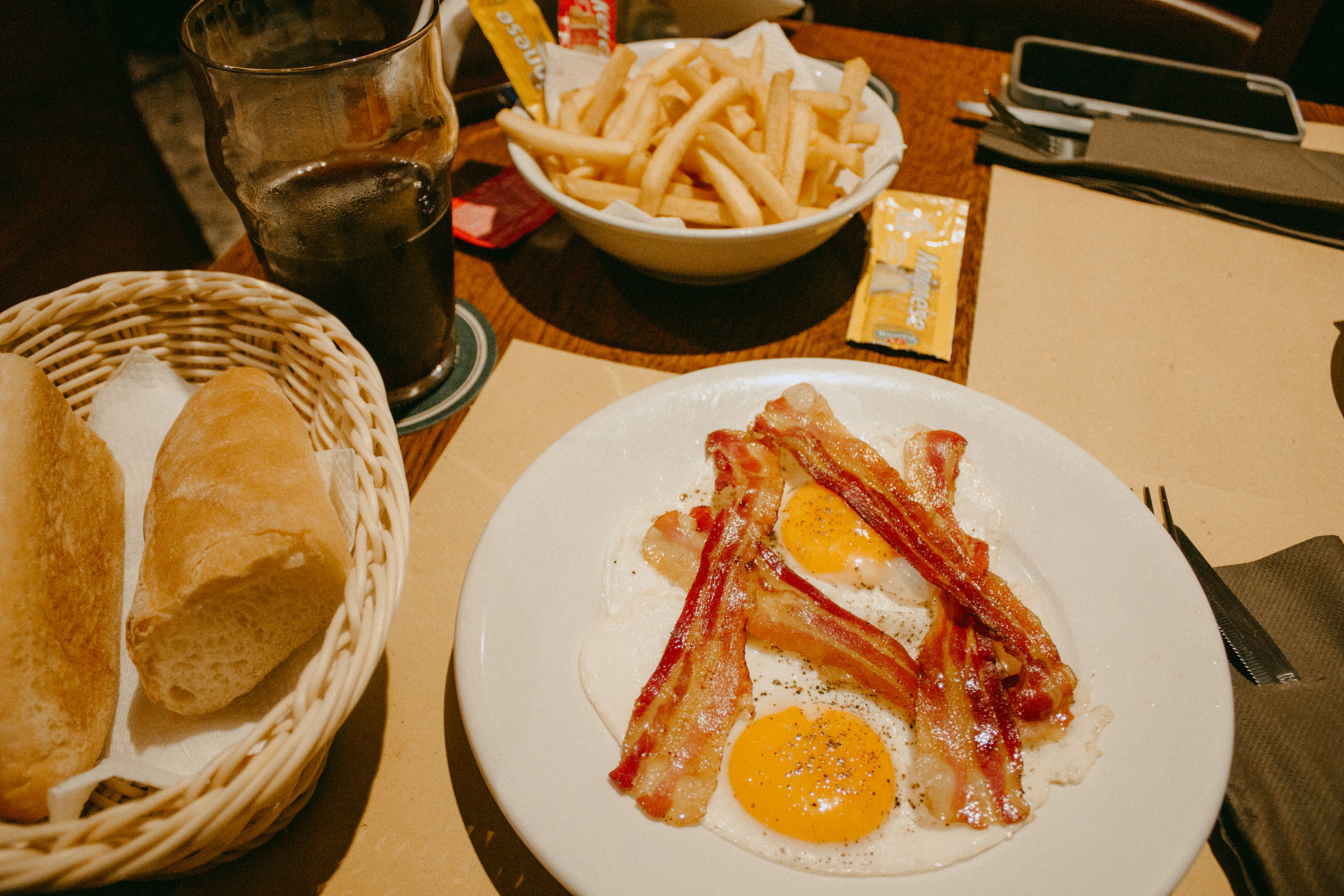 a white plate topped with bacon and eggs next to a basket of french fries