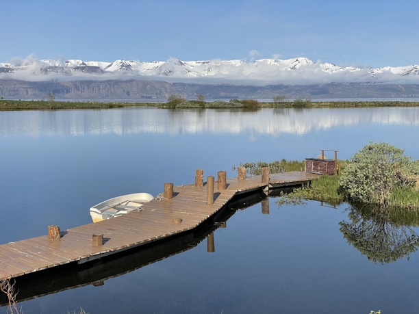 A wooden dock stretching into calm lake waters with a small rowboat tied up, framed by mountains.
