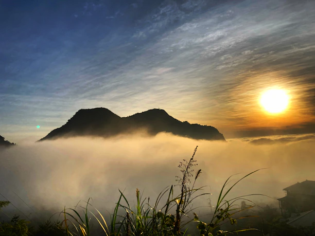 Sunrise over the lush slopes of Mount Meru with mist curling through the forest.