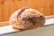 A freshly baked loaf of bread with a rustic crust, resting on a tiled surface. The bread has a golden-brown, crispy exterior with visible flour dusting and charred marks.