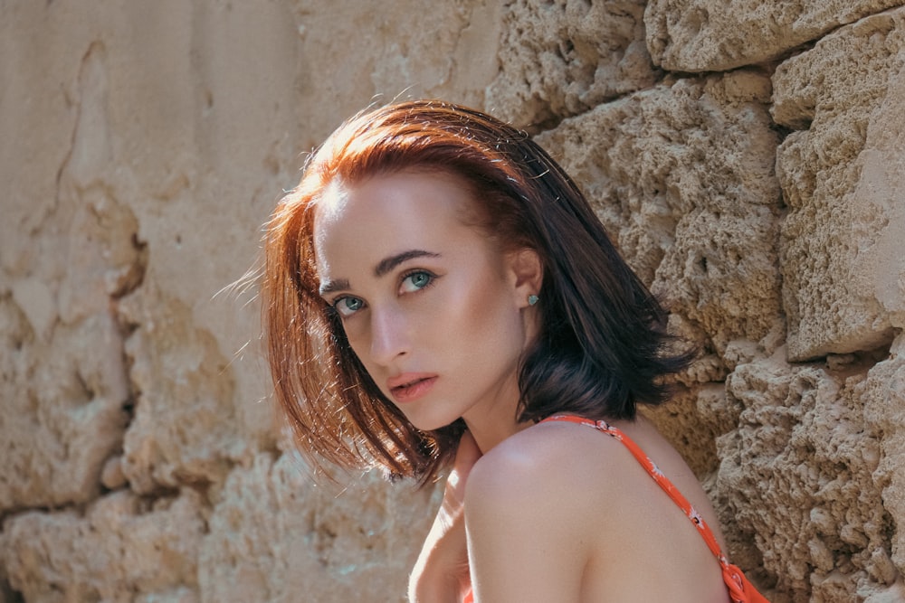 a woman in an orange dress leaning against a stone wall