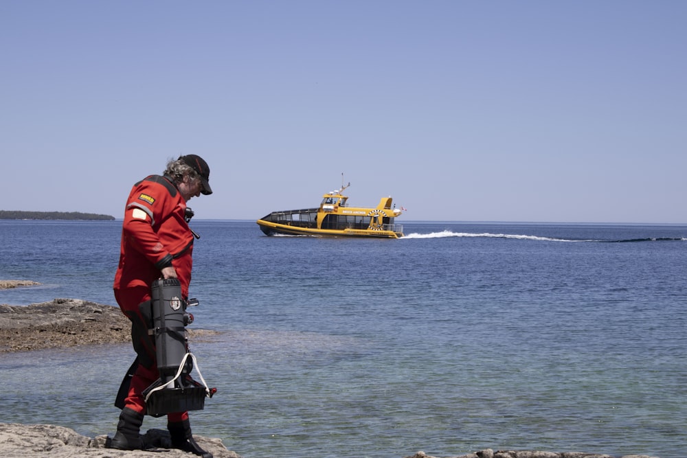 a man in a red suit standing on a rock next to a yellow boat