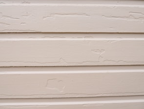 Several horizontal beige siding panels with visible signs of peeling paint and surface wear.