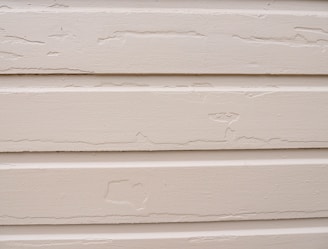Several horizontal beige siding panels with visible signs of peeling paint and surface wear.