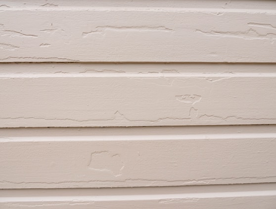 Several horizontal beige siding panels with visible signs of peeling paint and surface wear.