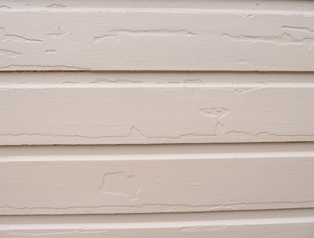 Several horizontal beige siding panels with visible signs of peeling paint and surface wear.