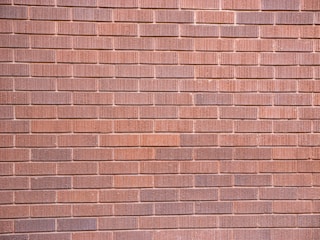 A wall constructed with uniformly sized brownish-red bricks arranged in a horizontal pattern. The brick texture is visible, with slight variations in color and surface detailing on each brick.