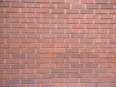A wall constructed with uniformly sized brownish-red bricks arranged in a horizontal pattern. The brick texture is visible, with slight variations in color and surface detailing on each brick.