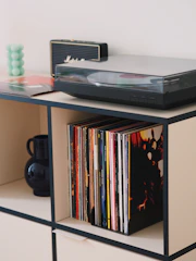 An industrial metal media stand with sleek lines holding a vintage record player and stacked books.