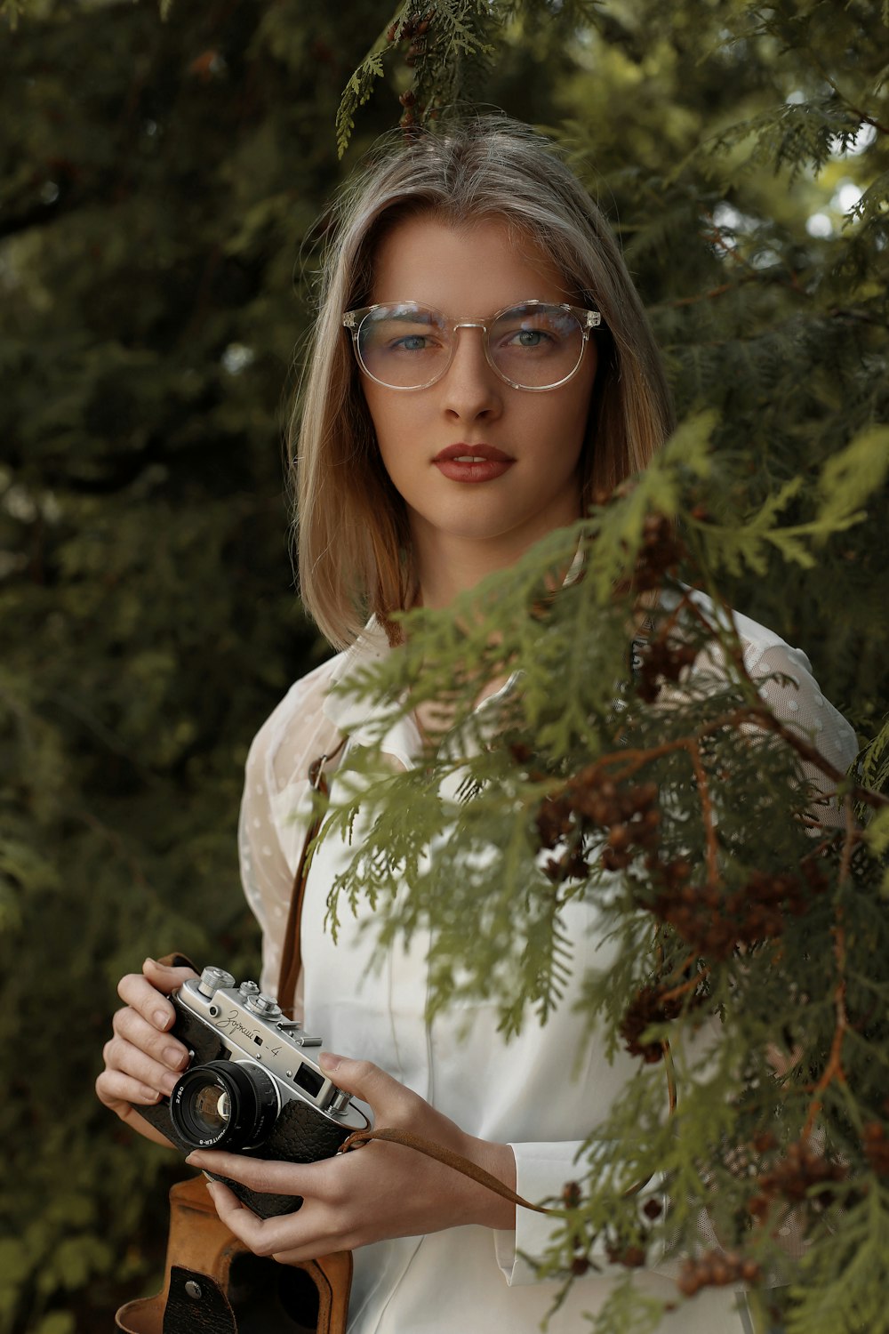 a woman wearing glasses holding a camera in front of a tree