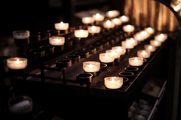 Close-up of neatly arranged tealight and votive candles glowing softly on a wooden table.