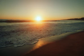 A cinematic shot of a sunset over a tropical beach, with soft cream skies and calm waves.