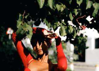 a woman in a red dress is standing under a tree