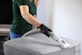 a woman in a green shirt and black gloves vacuuming a gray ottoman