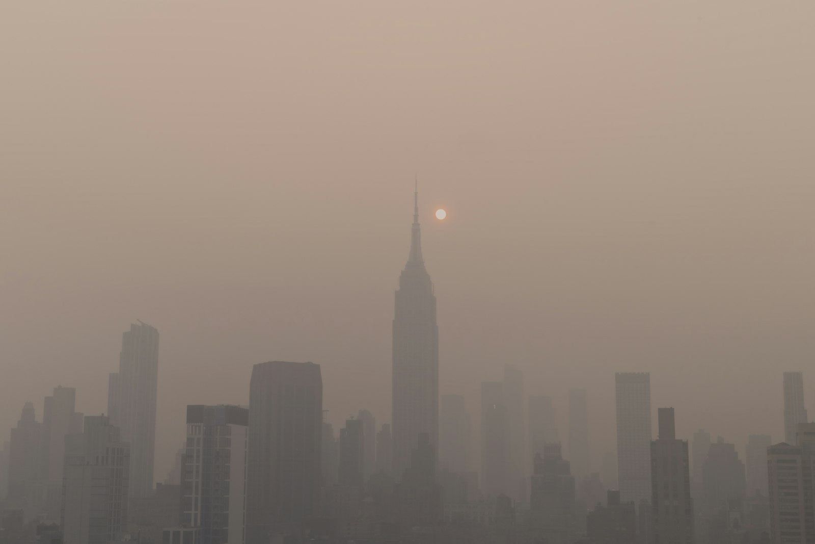 A city skyline dissolving into thick haze under a dim sun