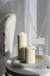 A cozy scene featuring aromatic candles and body mists with soft pink and green packaging on a white-cream background.