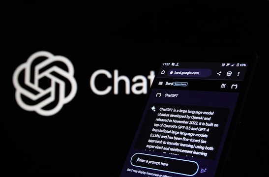 A smartphone displays a webpage related to ChatGPT, showcasing details about the language model and its development. The screen shows text explaining ChatGPT's capabilities and origins. In the background, a logo with a neural network design and the word 'ChatGPT' are visible.