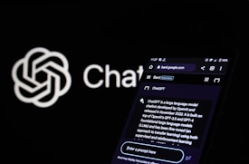 A smartphone displays a webpage related to ChatGPT, showcasing details about the language model and its development. The screen shows text explaining ChatGPT's capabilities and origins. In the background, a logo with a neural network design and the word 'ChatGPT' are visible.