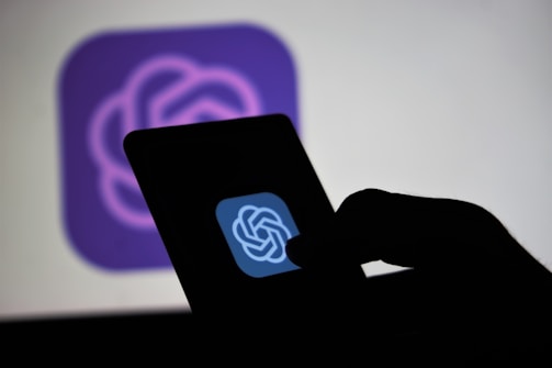 A hand holding a mobile device with a logo displayed on the screen, set against a blurred backdrop of the same logo.