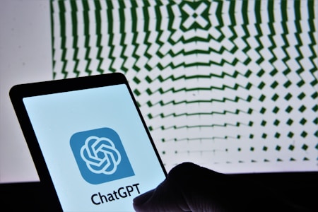 A smartphone displaying the ChatGPT logo is held against a backdrop of a geometric pattern, which consists of wavy, radial green lines that create an illusion of depth.