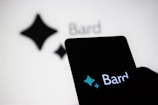 An illuminated smartphone screen displaying the word 'Bard' and a stylized four-pointed star logo. The same text and logo are also visible, though blurred, in the background.