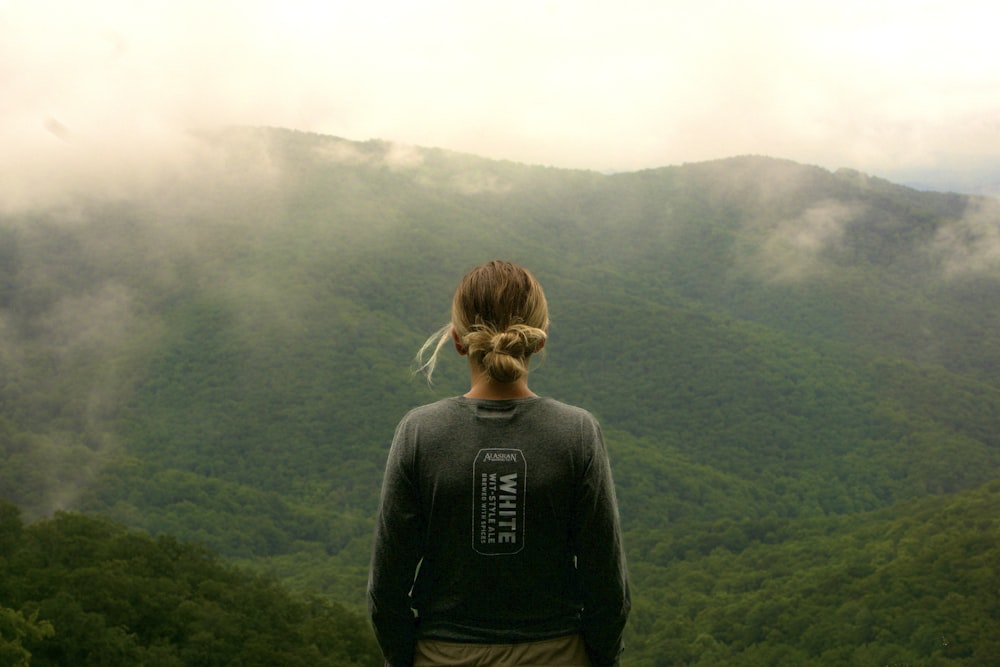 a woman standing on top of a lush green hillside