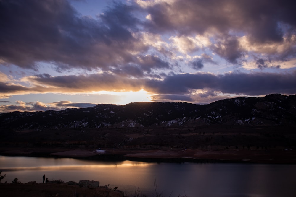 a lake surrounded by mountains under a cloudy sky